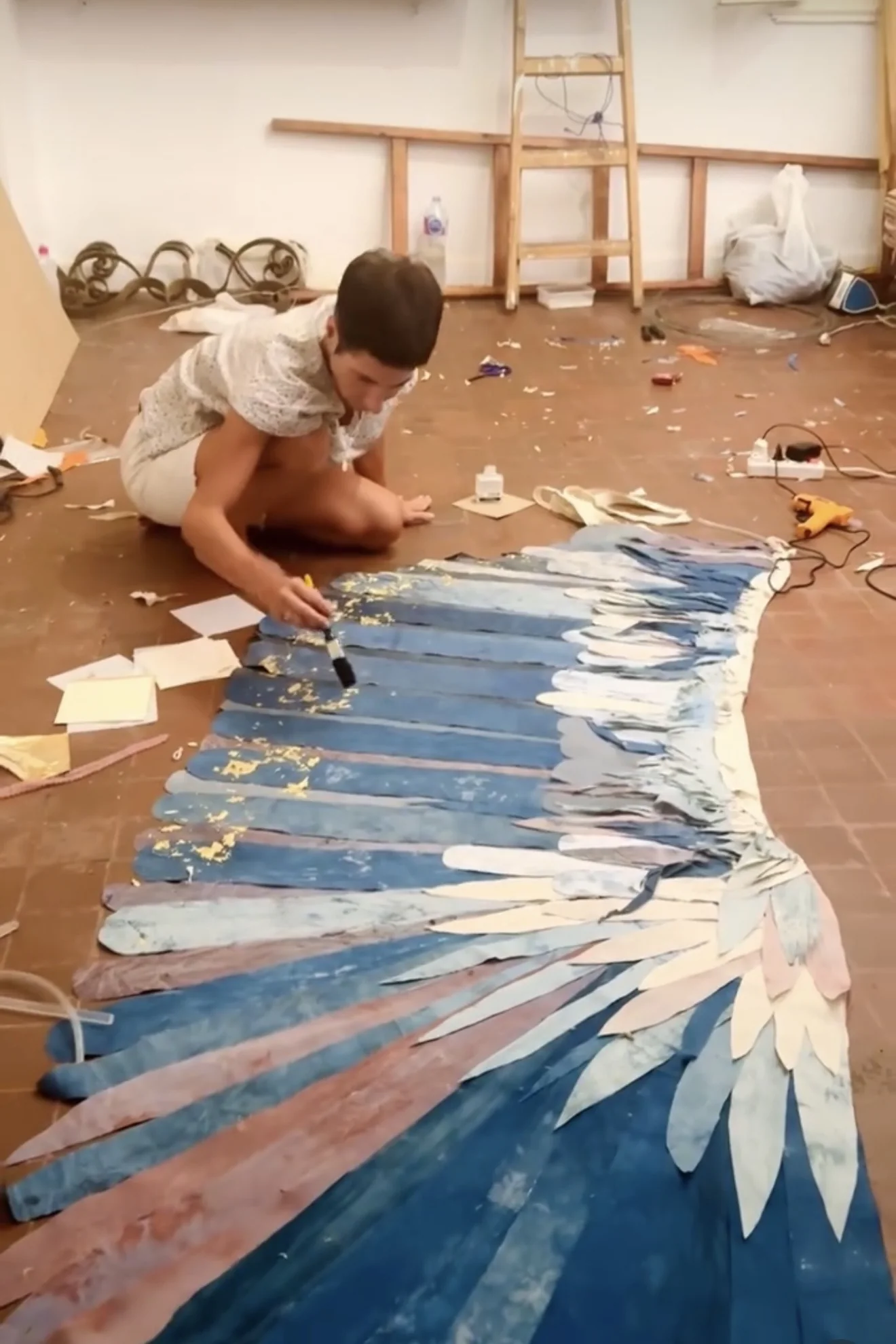 Esmeralda Kosmatopoulos applying gold leaf to a textile wing on the studio floor
